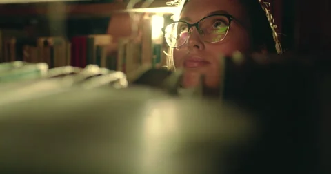 View through the library shelf of a girl in glasses viewing a library books Video stock 130302579