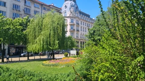 View through a lush green park and colorful flower garden toward a distinctive Stock Footage 328214759