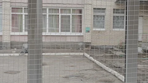 View through a metal mesh fence of an old, abandoned brick building Stock Footage 346547441