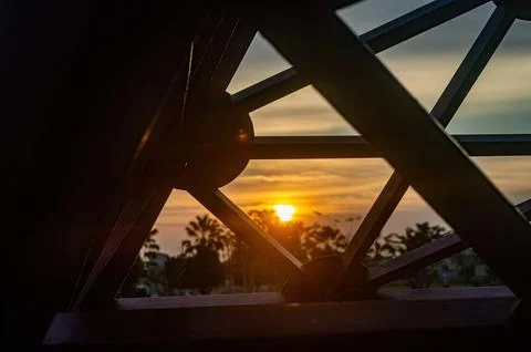 View through a metal structure reveals a vibrant sunset over a tropical lan.. Stock-Fotos