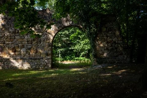 View through an old stone arch of a ruined historical building to a forest Foto stock