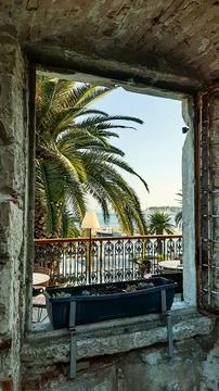 View through the old window of the stone house on palm trees, sea and yacht Stock Photos