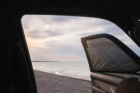 A view through an open car window with a sunshade towards a pebble beach and  Stock Photos