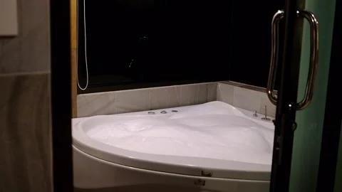 View through an open door of a white whirlpool bathtub filled with bubble foam Stock Footage 340234102