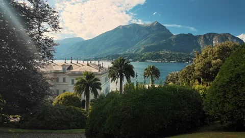 View through palm and greenery at Lake Como with elegant white building on shore Stock Footage 324839676
