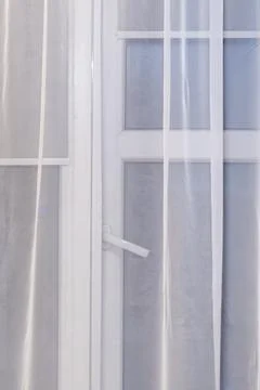 A view through a partially closed white curtain covering a window, with soft Stock Photos