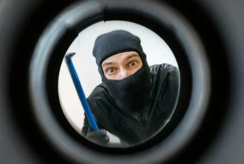 View through pipehole. Thief or burglar masked with balaclava is holding crowbar Stock-Fotos