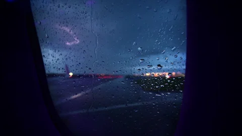View through a rain-covered airplane window at dusk over a wet tarmac with Stock Footage 342276925