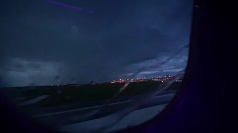 View through a rain-streaked airplane window of blurred airport lights at night, Stock Footage 342249938