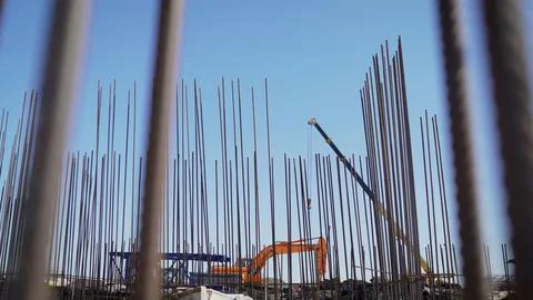 View through rebar cage at active construction site. Orange excavator and cra Stock Photos
