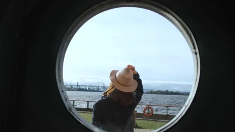 View through a round window of a girl with a hat on a cold day by the water Stock Footage 144073544
