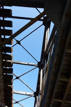 View through structural components of old railway bridge to blue sky above Stock Photos