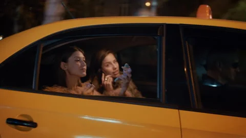 View Through Taxi Window of Two Stylish Girls Putting on Makeup and Talking Stock Footage 319777045