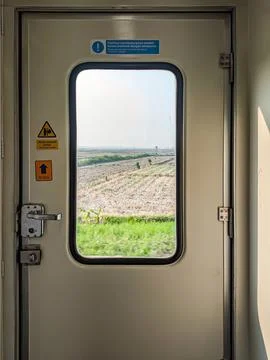 A view through a train door window showing a scenic landscape of fields and.. Stock Photos
