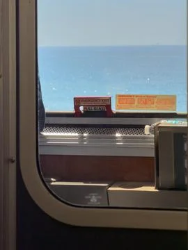 View through a train window showing the Pacific Ocean, with emergency exit sign Stock Photos