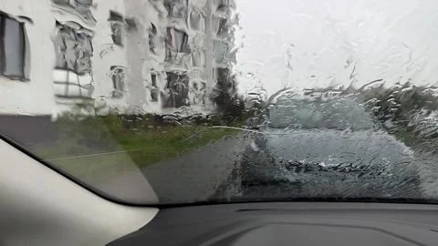 View through a wet car windshield covered in rain drops focusing on a blurred Stock Photos