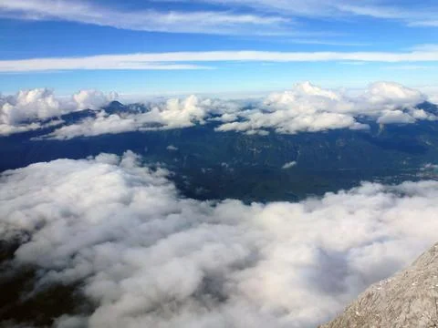 View through white clouds to mountain peaks and blue sky above them Stock Photos
