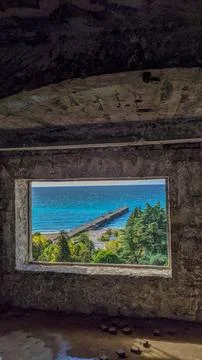 View through the window of an abandoned building showing a sea pier and green Stock Photos