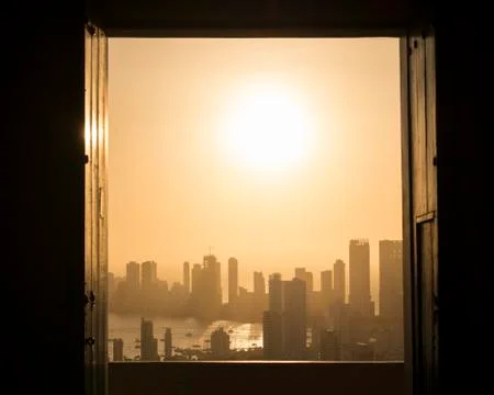 View through a window across the cityscape and seafront with misty orange sky Stock Photos