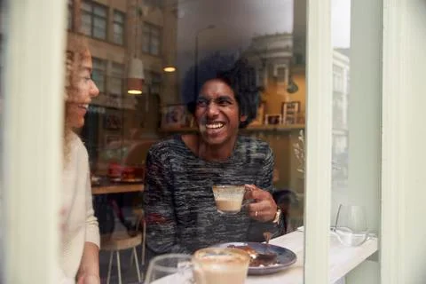 View Through Window Of Couple Enjoying Drink In Coffee Shop Foto stock
