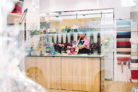 A view through the window of a flower shop and a florist's girl making bouquets Stock Photos