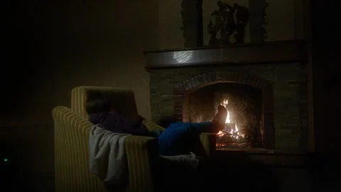 View through window of girl warming feet by fireplace Stock Footage 321957721