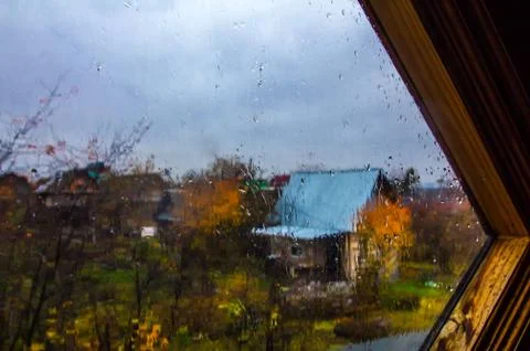 View through window glass covered with raindrops into autumn garden Stock Photos