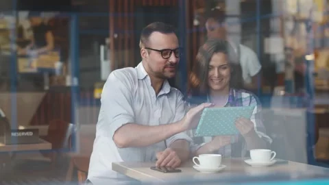 View through window of smiling young couple looking at digital tablet with Stock Footage 134547468