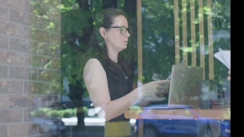 View through window woman black blouse glasses works office cafe city street day Stock Footage 246714334