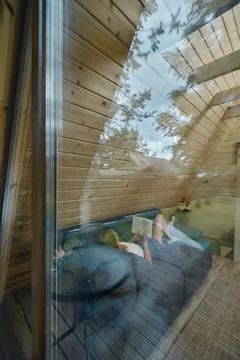 View through the window at a woman on sofa inside summer house reading a book Foto stock