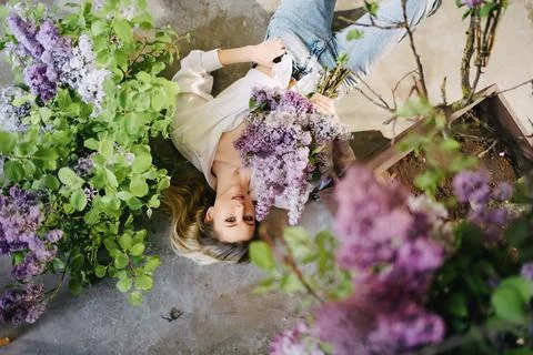 View top. a blonde in a white shirt and jeans on the floor with lilac flowers. Foto stock