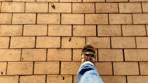 View from the top of the legs of a man walking along a brown clinker pavement. Stock Footage 143477173