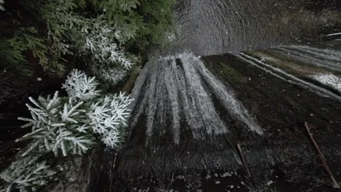 View from Top of Small Waterfall Dam While Snowing with Nature Around Stock Footage 304264599