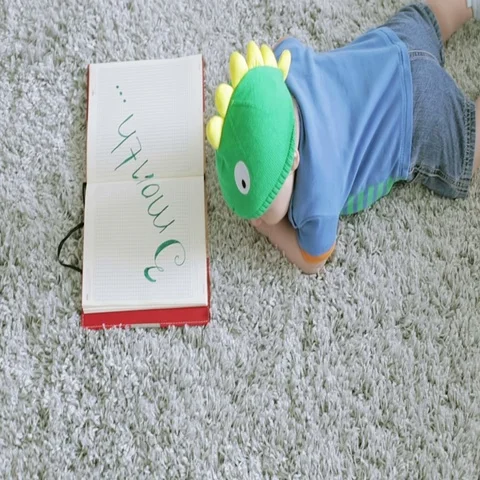 View from the top. Three-month baby in a green dragon form hat looks in notebok. Stock Footage 69301088