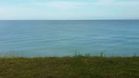 View from train window. Movement along sea, green grass, station and bright sky. Stock Footage 221354139