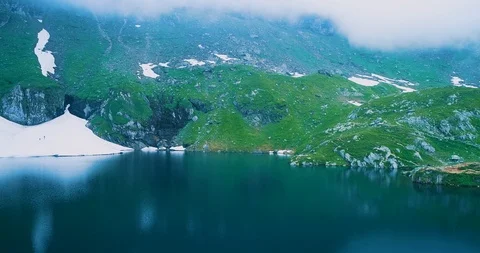 View of Transfagarash lake at the bottom of hill with snow and two tourists Stock Footage 127091488
