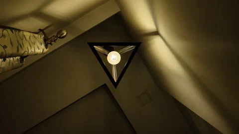 Up view to a triangle lamp in a room, making gold light and shadow pattern Stock Footage 279532716