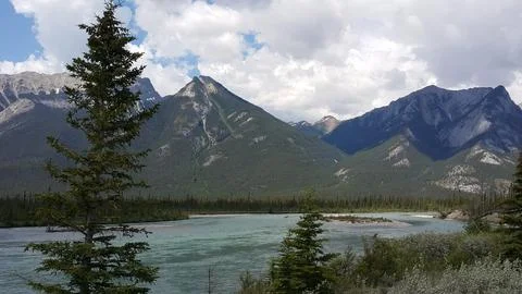 View of turquoise river winding through pine forest with rugged mountain peaks. Stock Photos