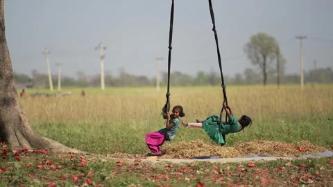 View of two girls playing on a swing in a rural field, Nepal. Stock Footage 335476816