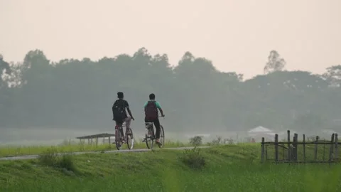 View of two people riding bicycles on a rural path, Bangladesh. Video stock 334968441