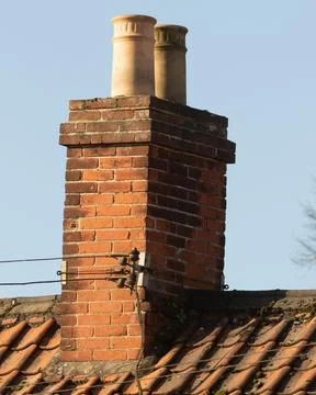 View of two weathered cream chimney pots on a red brick chimney stack and roof a Stock Photos