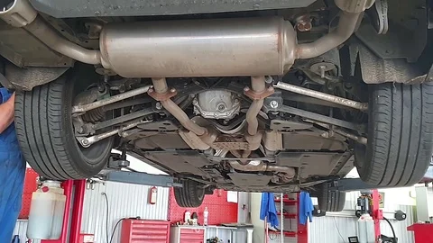 View under bottom of car raised on lift in car workshop, mechanic checks wheels 스톡 동영상 123775613