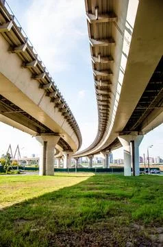 View under bridge over river, cityscape, bright day and green grass, blue sky Stock Photos