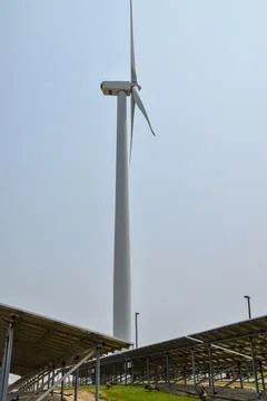 View from underneath an array of solar panels with a wind farm wind turbine  Stock Photos