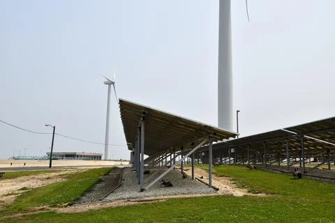 View from underneath an array of solar panels with a wind farm wind turbine  Stock Photos