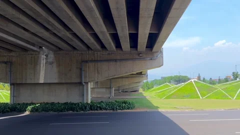 View from underneath a massive concrete flyover bridge with park background Stock Footage 324746858