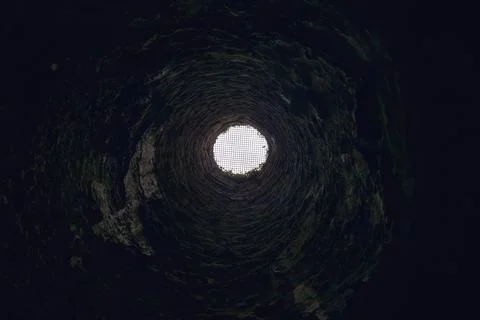 View upward from inside a deep stone well toward a bright circular opening .. Stock Photos