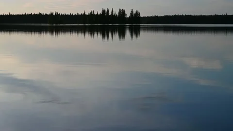View of a very calm lake that is reflecting a blue sky with white clouds.  Stock Footage 231229014
