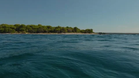 View from water surface looking at gentle sea waves and pine tree coastline 库存影片 348239329