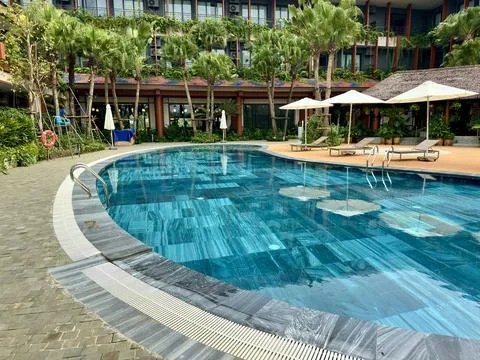 View from water surface towards sun loungers and thatched roof area Stock Photos